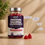 A bottle of Pact Nutrition Biotin Gummies in natural strawberry flavour, shown on a wooden surface with two loose gummies in front. White callout lines with text highlight key features: 10,000μg biotin per serving, natural strawberry flavour, easy to chew, and 30 servings.